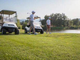 Terrain de golf, avec deux golfeurs devant leurs voitures de golf. On aperçoit un lac à l'arrière.