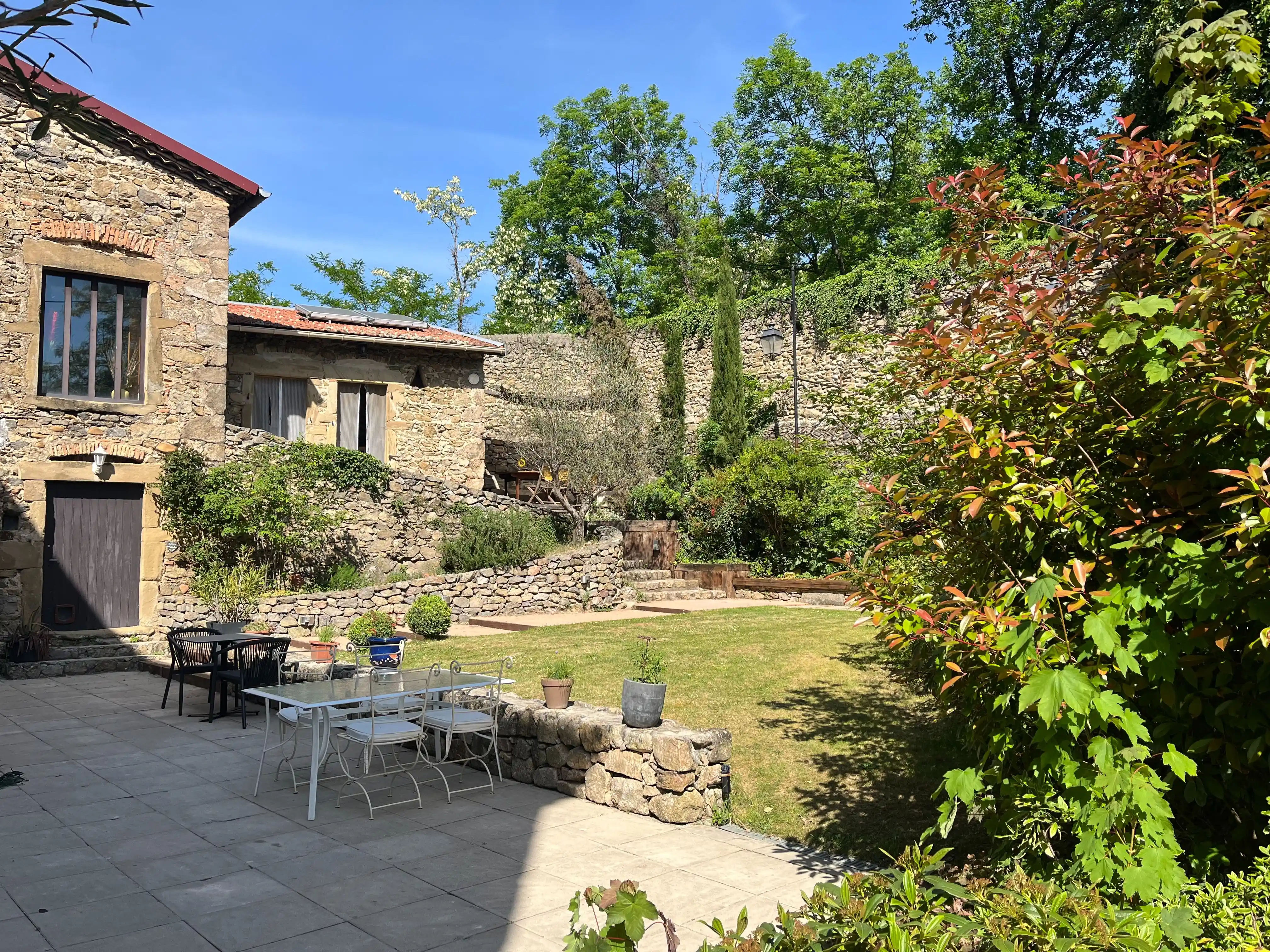 Cour intérieure du Domaine de Pipangaille entourée de murs en pierre, avec terrasse ombragée et escalier menant aux chambres