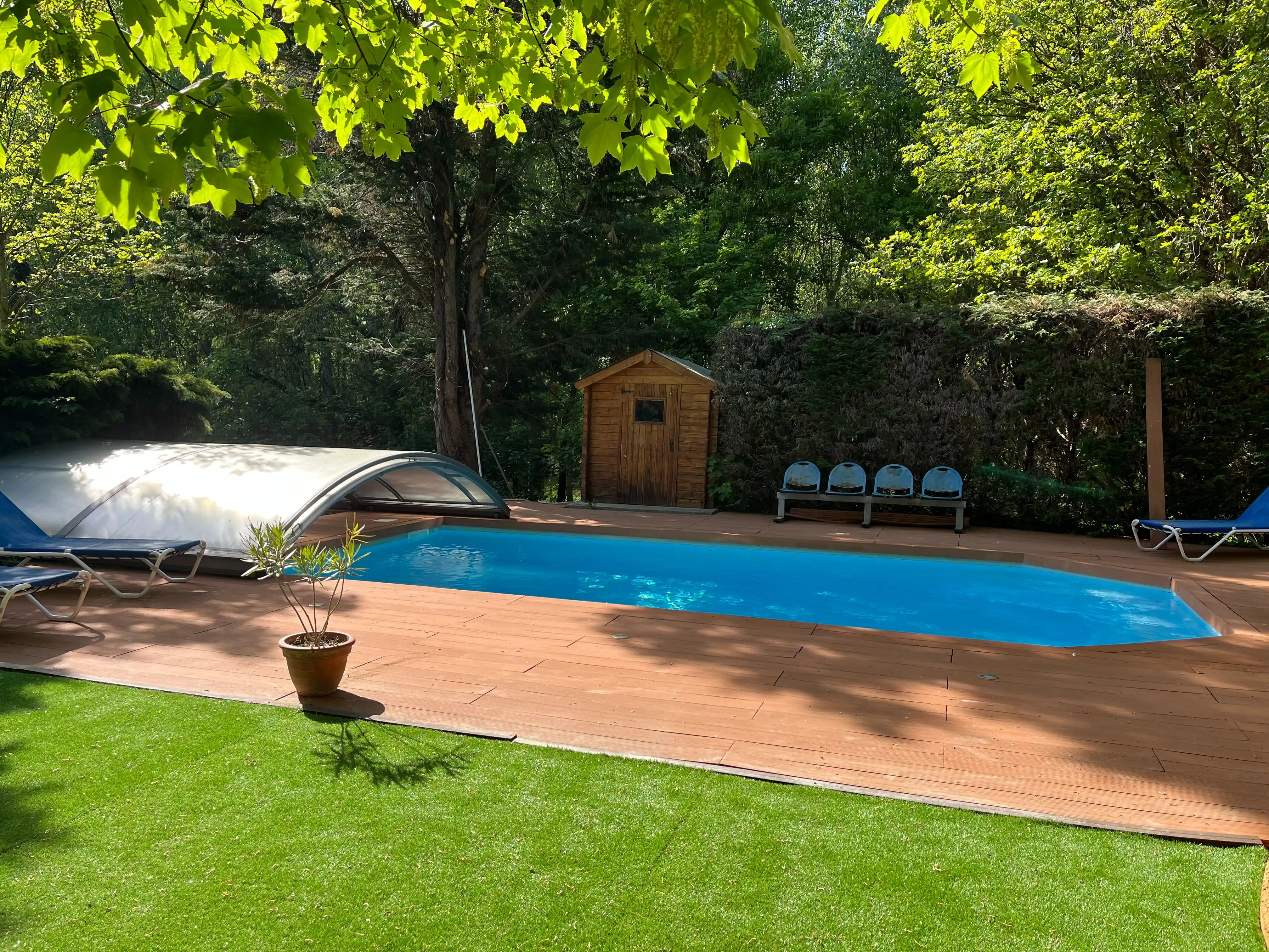 Buitenzwembad van het Domein Pipangaille omgeven door bomen, met houten terras en kunstgrasgebied.