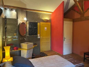 Chambre à thématique africaine de couleur grise et ocre, sur lequel nous voyons un lavabo, la porte de la chambre…