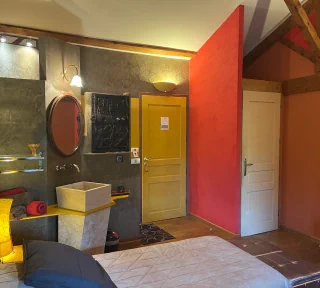Chambre à thématique africaine de couleur grise et ocre, sur lequel nous voyons un lavabo, la porte de la chambre…