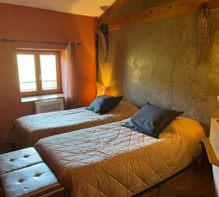Chambre à thématique africaine de couleur grise et ocre avec disposition de deux lits simples. Avec par la fenêtre, vue sur le jardin.