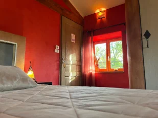 Une jolie photo de la chambre marocaine, en premier plan, un fondu du joli dessus-de-lit. Au fond de l'image la porte de la chambre au centre et à droite la vue par la fenêtre sur le bois et la cour intérieure