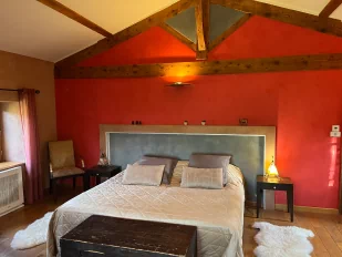 Chambre thématique marocaine. Aux couleurs rouge, ocre et gris. Nous voyons un lit king size recouvert d'un beau dessus-de-lit couleur or.