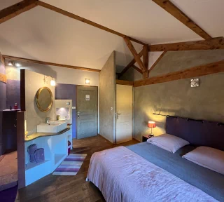 Photo de la Chambre toscane, aux couleurs grise et violette. On aperçoit un grand lit double, la belle douche faite de matériaux nobles et l'lavabo sur sa droite.