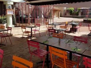 Terrasse de restaurant ombré, table dressée en bois et chaise de couleur orange et rose.