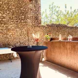 Une table recouverte d'un tissus noir joliment decoré au premier plant, en fond le mur en pierre du préau.